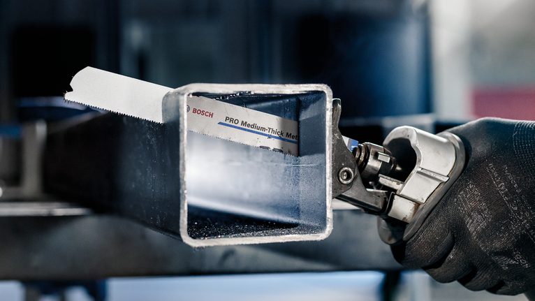 บุคคลที่สวมอุปกรณ์ความปลอดภัยกำลังตัดท่อโลหะสี่เหลี่ยมด้วยเลื่อยไฟฟ้า