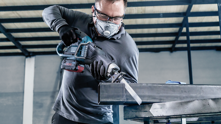 บุคคลที่สวมอุปกรณ์ความปลอดภัยกำลังตัดคานโลหะด้วยเลื่อยตัดโลหะแบบลูกสูบ