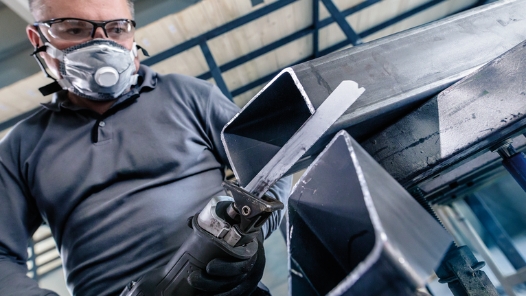 บุคคลที่สวมอุปกรณ์ความปลอดภัยกำลังตัดคานโลหะด้วยเลื่อยตัดโลหะแบบลูกสูบ