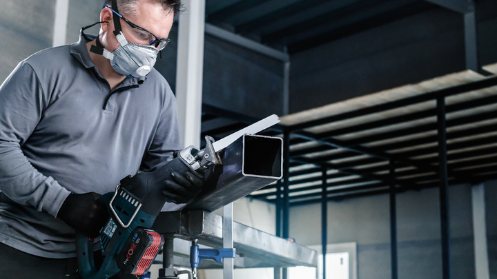 บุคคลที่สวมอุปกรณ์ความปลอดภัยกำลังตัดท่อโลหะด้วยเลื่อยตัดโลหะแบบลูกสูบ