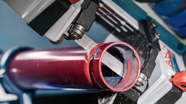 ใบเลื่อย PRO CB2824 Band, 733 มม., 2 ชิ้น เลื่อยสายพานกำลังตัดผ่านท่อโลหะสีแดงในโรงงานแห่งหนึ่ง