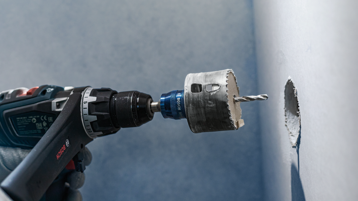 บุคคลที่สวมอุปกรณ์ความปลอดภัยกำลังเจาะรูวงกลมในผนังด้วยเลื่อยเจาะรู