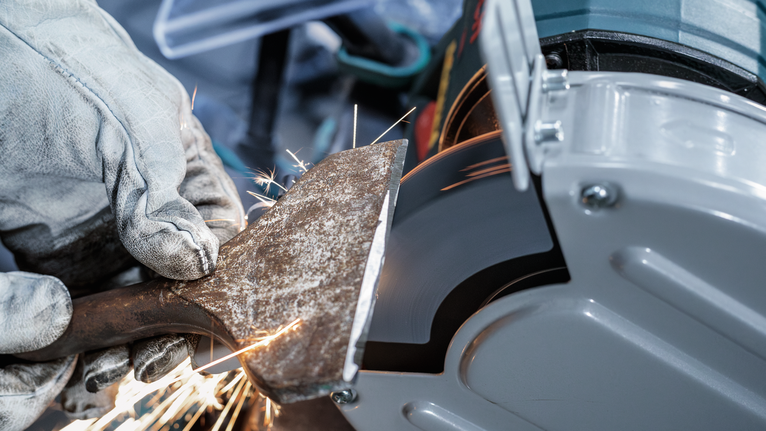 บุคคลที่สวมอุปกรณ์ป้องกันความปลอดภัยกำลังบดโลหะด้วยเครื่องมือไฟฟ้าในขณะที่มีประกายไฟพุ่งออกมา