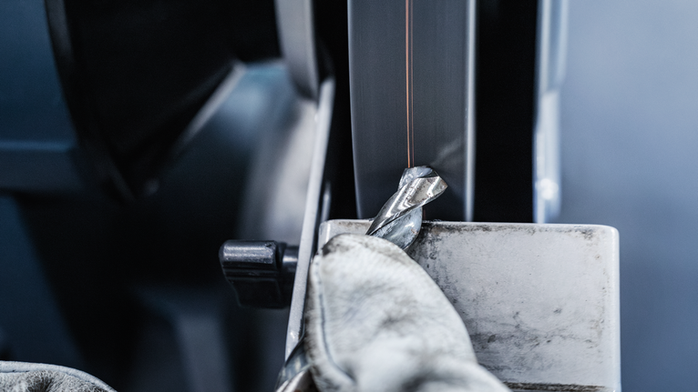 บุคคลที่สวมอุปกรณ์ความปลอดภัยกำลังลับคมดอกสว่านโลหะบนเครื่องเจียรแท่น