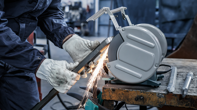 บุคคลที่สวมอุปกรณ์ด้านความปลอดภัยกำลังเจียรโลหะด้วยเครื่องเจียรแท่น ทำให้เกิดประกายไฟ