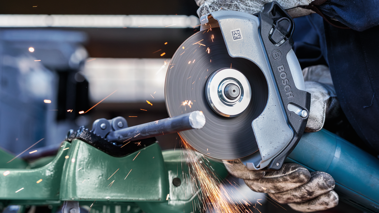 บุคคลที่สวมอุปกรณ์ป้องกันความปลอดภัยตัดแท่งโลหะด้วยเครื่องเจียรแบบมุมหมุน