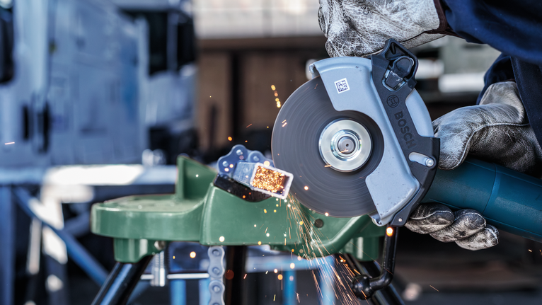 บุคคลที่สวมอุปกรณ์ความปลอดภัยตัดท่อโลหะด้วยเครื่องเจียร มีประกายไฟกระเด็นออกมา