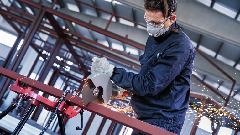 บุคคลที่สวมอุปกรณ์ความปลอดภัยใช้เครื่องตัดไฟฟ้าตัดท่อโลหะ ทำให้เกิดประกายไฟ