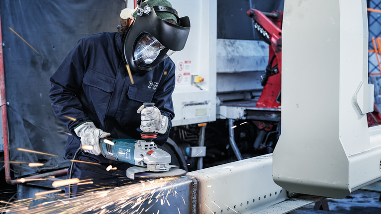 บุคคลที่สวมอุปกรณ์ด้านความปลอดภัยใช้เครื่องเจียรตัดคานโลหะ
