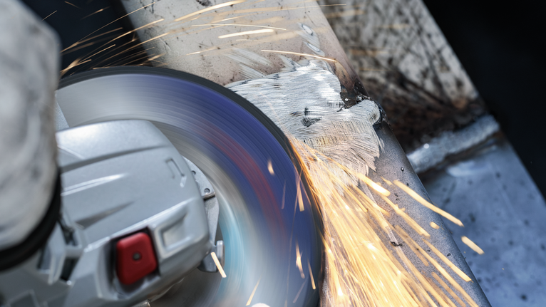 บุคคลที่สวมอุปกรณ์ความปลอดภัยทำการเจียรพื้นผิวโลหะ ทำให้เกิดประกายไฟสว่าง