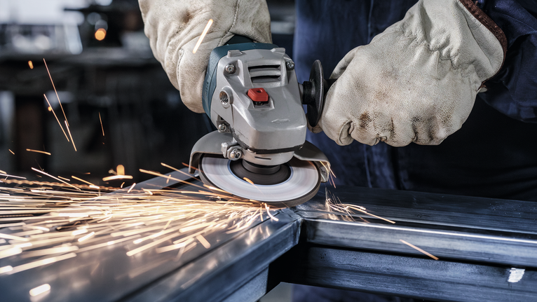 บุคคลที่สวมอุปกรณ์ป้องกันความปลอดภัยทำการบดโลหะ ทำให้เกิดประกายไฟสว่าง.