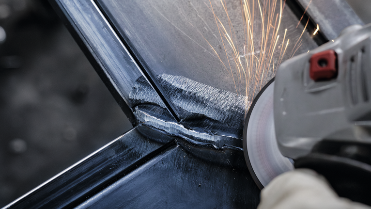 บุคคลที่สวมอุปกรณ์ป้องกันความปลอดภัยกำลังเจียรเชื่อมโลหะ ทำให้เกิดประกายไฟ.