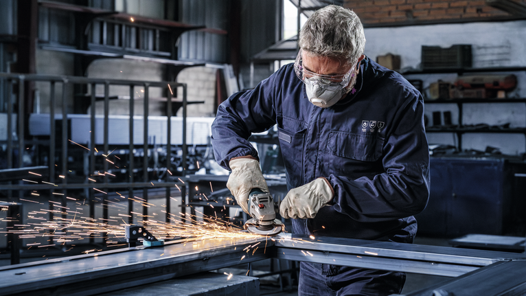 บุคคลที่สวมอุปกรณ์ความปลอดภัยกำลังบดโลหะ ทำให้เกิดประกายไฟในโรงงาน.