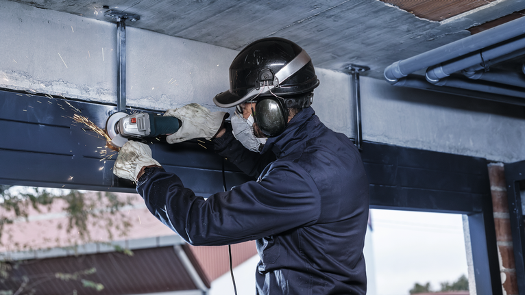 บุคคลที่สวมอุปกรณ์ความปลอดภัยบดคานโลหะทำให้เกิดประกายไฟ