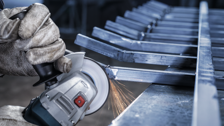 บุคคลที่สวมอุปกรณ์นิรภัยกำลังบดแท่งโลหะด้วยเครื่องเจียร ทำให้เกิดประกายไฟ