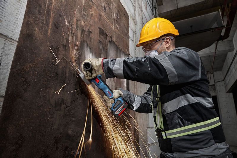 บุคคลที่สวมอุปกรณ์ด้านความปลอดภัยกำลังเจียรแผ่นโลหะที่เป็นสนิมด้วยเครื่องเจียรไร้สาย.