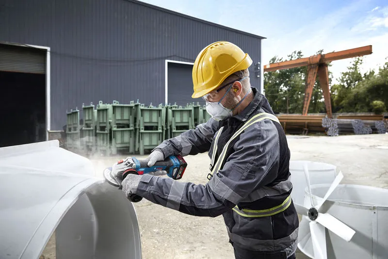 บุคคลที่สวมอุปกรณ์ด้านความปลอดภัยกำลังบดโลหะกลางแจ้งในพื้นที่อุตสาหกรรม.