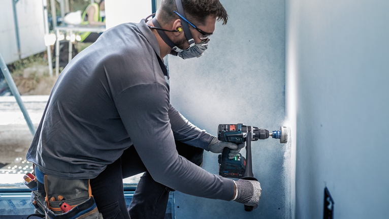 บุคคลที่สวมอุปกรณ์ความปลอดภัยกำลังเจาะรูวงกลมในกำแพง