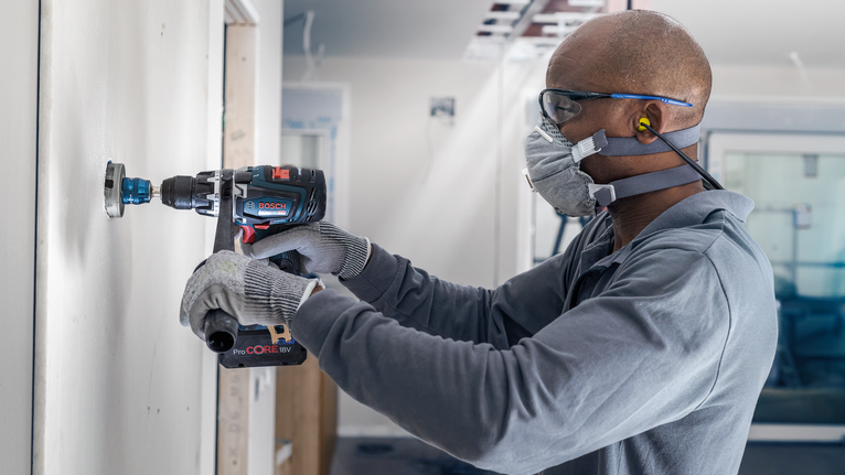 บุคคลที่สวมอุปกรณ์ความปลอดภัยกำลังเจาะรูวงกลมในผนัง