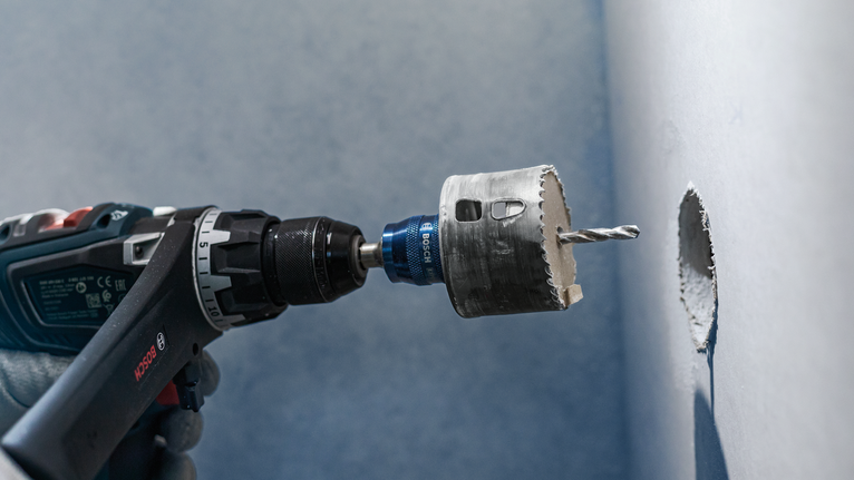 บุคคลที่สวมอุปกรณ์ความปลอดภัยกำลังเจาะรูวงกลมในผนังด้วยเลื่อยเจาะรู