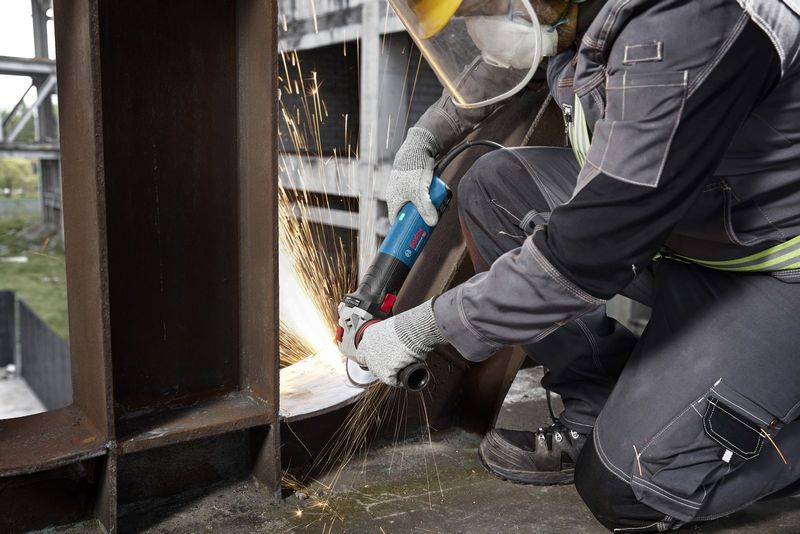 บุคคลที่สวมอุปกรณ์ความปลอดภัยกำลังเจียรคานโลหะด้วยเครื่องเจียรแบบมุม.