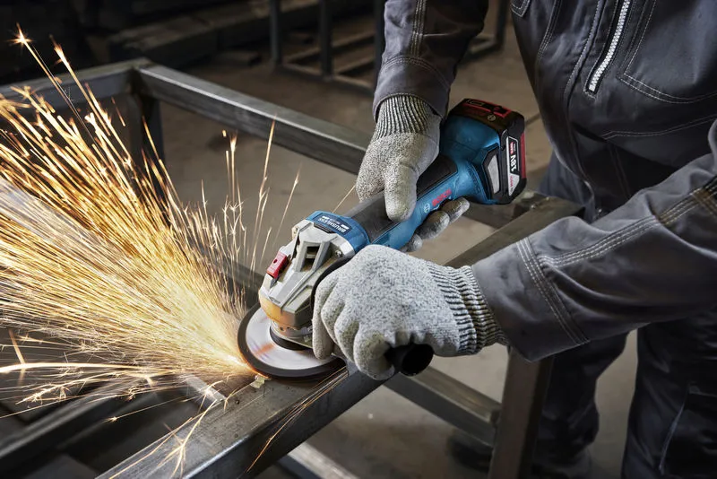 บุคคลที่สวมอุปกรณ์ความปลอดภัยกำลังเจียรคานโลหะด้วยเครื่องเจียรแบบมุม.