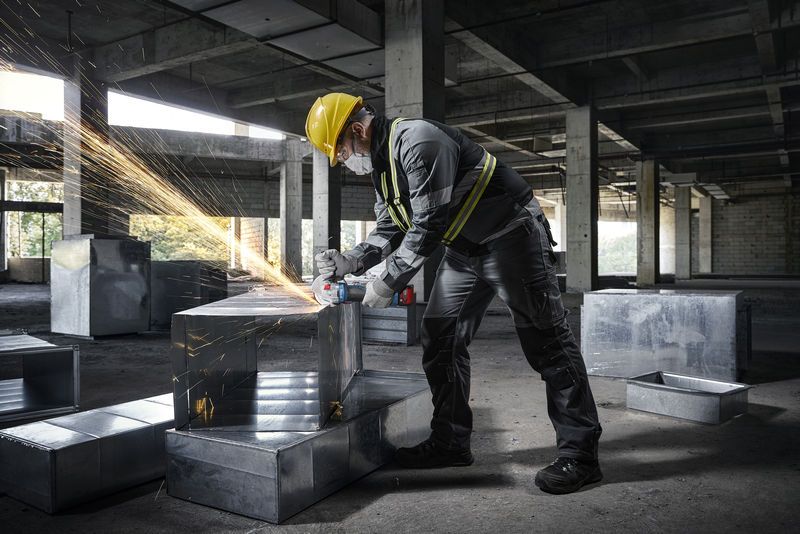 บุคคลที่สวมอุปกรณ์ด้านความปลอดภัยใช้เครื่องเจียรกับท่อโลหะในไซต์ก่อสร้าง.