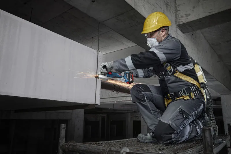 บุคคลที่สวมอุปกรณ์ความปลอดภัยกำลังบดคอนกรีตด้วยเครื่องมือไฟฟ้าในไซต์ก่อสร้าง.