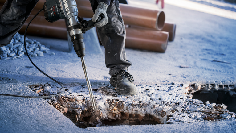 บุคคลที่สวมอุปกรณ์ป้องกันความปลอดภัยทุบพื้นคอนกรีตด้วยเครื่องมือไฟฟ้าที่ใช้งานหนัก