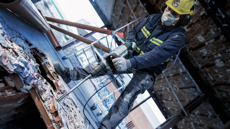 บุคคลที่สวมอุปกรณ์ความปลอดภัยกำลังเจาะเข้าไปในคอนกรีตที่ไซต์ก่อสร้าง