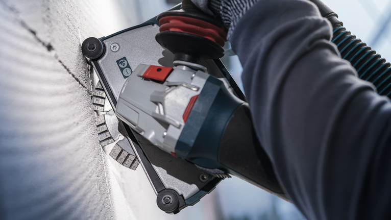 บุคคลที่สวมอุปกรณ์ความปลอดภัยกำลังบดผนังด้วยเครื่องมือไฟฟ้า