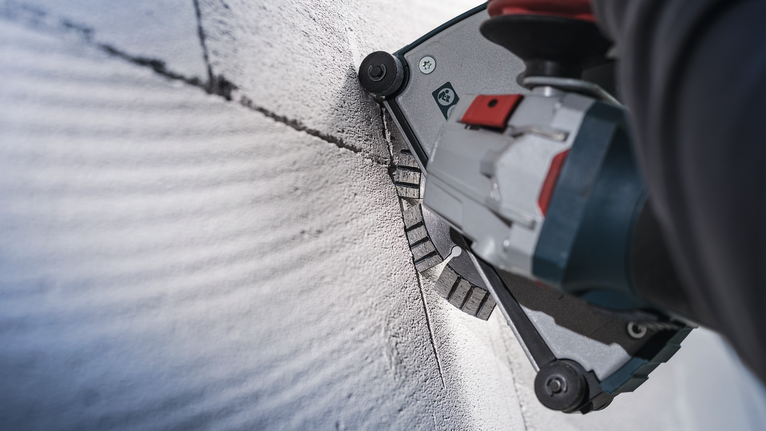 บุคคลที่สวมอุปกรณ์ความปลอดภัยใช้เครื่องมือไฟฟ้าตัดร่องตรงในคอนกรีต