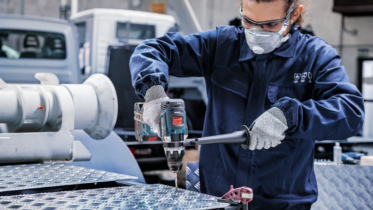 บุคคลที่สวมอุปกรณ์ด้านความปลอดภัยเจาะลงไปในพื้นผิวโลหะในสถานประกอบการอุตสาหกรรม