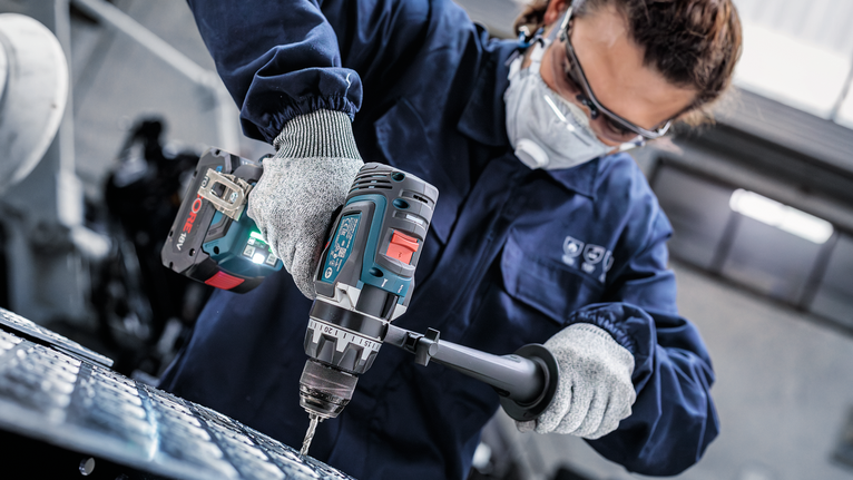 บุคคลที่สวมอุปกรณ์ความปลอดภัยกำลังเจาะเข้าไปในโลหะโดยใช้เครื่องมือไฟฟ้า