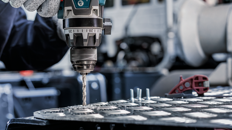 บุคคลที่สวมอุปกรณ์ความปลอดภัยกำลังเจาะรูบนแผ่นโลหะ