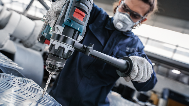 บุคคลที่สวมอุปกรณ์ความปลอดภัยกำลังเจาะแผ่นโลหะในโรงงานอุตสาหกรรม