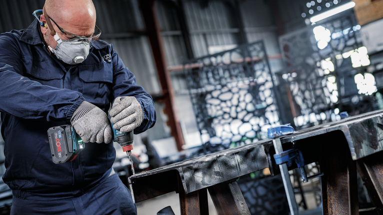 บุคคลที่สวมอุปกรณ์ความปลอดภัยกำลังเจาะคานโลหะภายในโรงงาน