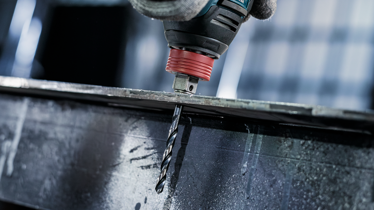 บุคคลที่สวมอุปกรณ์ความปลอดภัยกำลังเจาะผ่านคานโลหะ