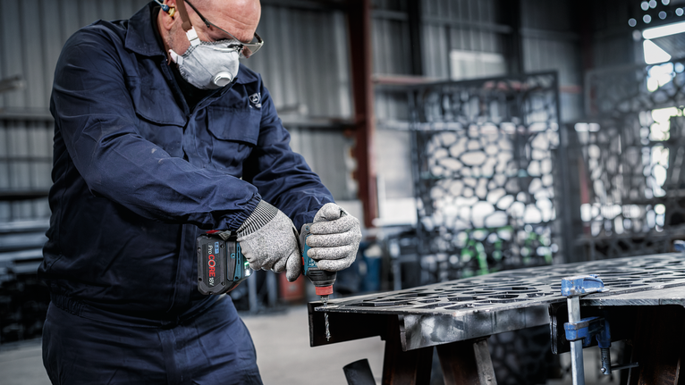 บุคคลที่สวมอุปกรณ์ความปลอดภัยกำลังเจาะแผ่นโลหะในโรงงาน