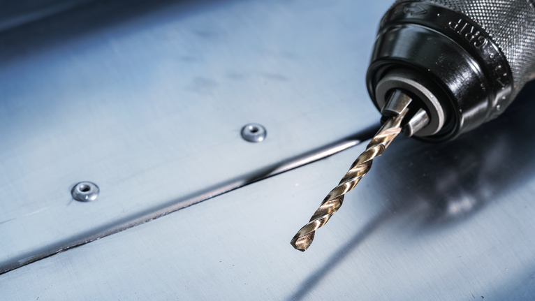 สว่านไฟฟ้าที่มีดอกสว่านโลหะวางอยู่บนแผ่นเหล็ก