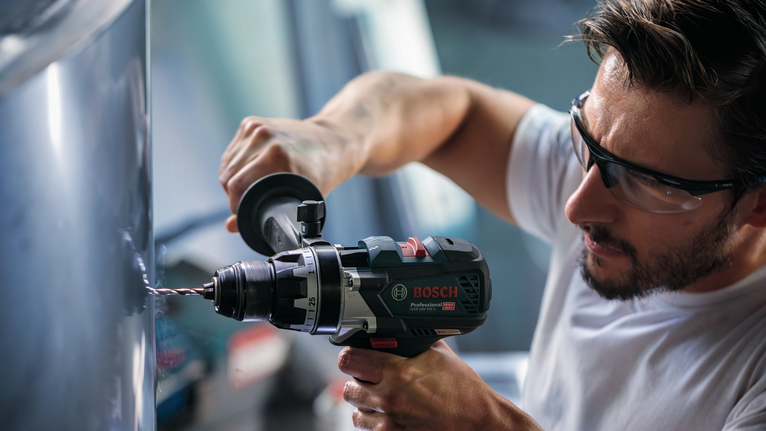 บุคคลที่สวมอุปกรณ์ความปลอดภัยกำลังเจาะเข้าไปในโลหะด้วยเครื่องมือไฟฟ้า