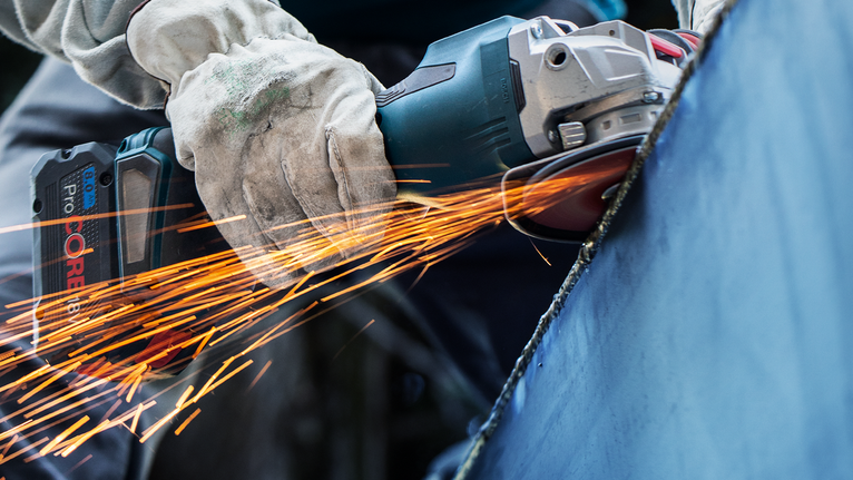 บุคคลที่สวมอุปกรณ์ป้องกันความปลอดภัยกำลังบดโลหะด้วยเครื่องมือไฟฟ้า ทำให้เกิดประกายไฟ