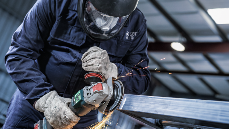 บุคคลที่สวมอุปกรณ์ความปลอดภัยทำการเจียรโลหะ ทำให้เกิดประกายไฟ