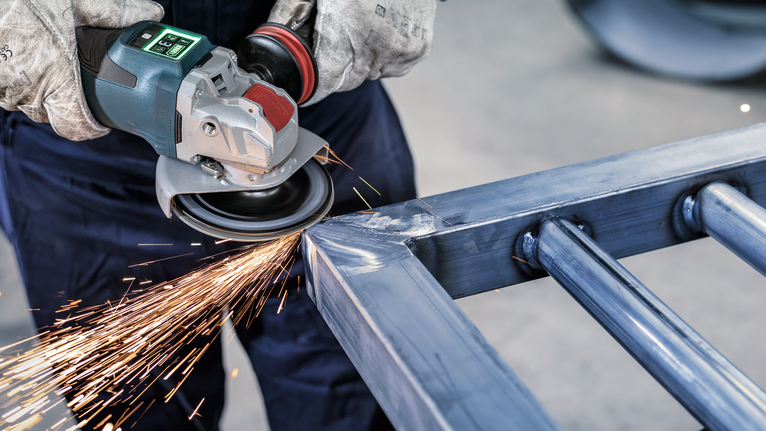 บุคคลที่สวมอุปกรณ์ความปลอดภัยทำการเจียรโลหะ ทำให้เกิดประกายไฟสว่าง