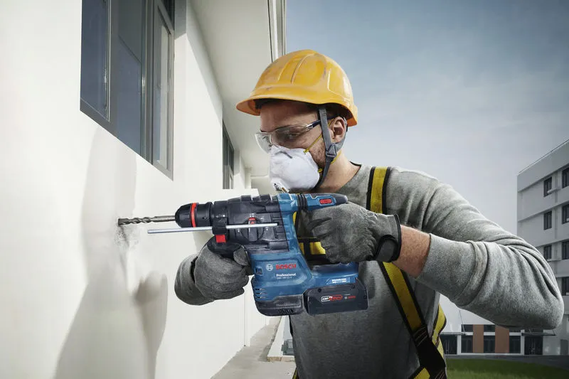 บุคคลที่สวมอุปกรณ์ด้านความปลอดภัยเจาะเข้าไปในผนังด้านนอกโดยใช้เครื่องมือไฟฟ้า.