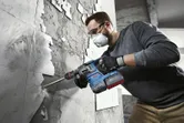 บุคคลที่สวมอุปกรณ์ด้านความปลอดภัยใช้ค้อนโรตารี่เพื่อดึงกระเบื้องออกจากผนัง.