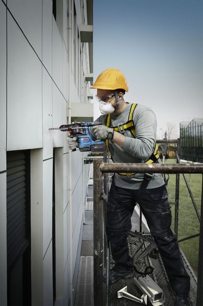 บุคคลที่สวมอุปกรณ์ด้านความปลอดภัยเจาะเข้าไปในผนังด้านนอกในขณะที่ยืนอยู่บนนั่งร้าน.