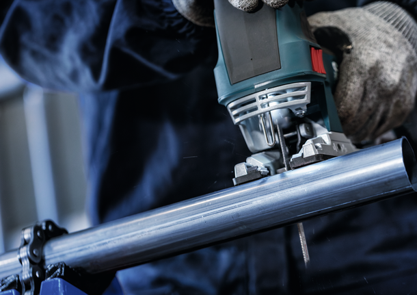 บุคคลที่สวมอุปกรณ์ความปลอดภัยใช้จิ๊กซอว์ตัดท่อเหล็ก