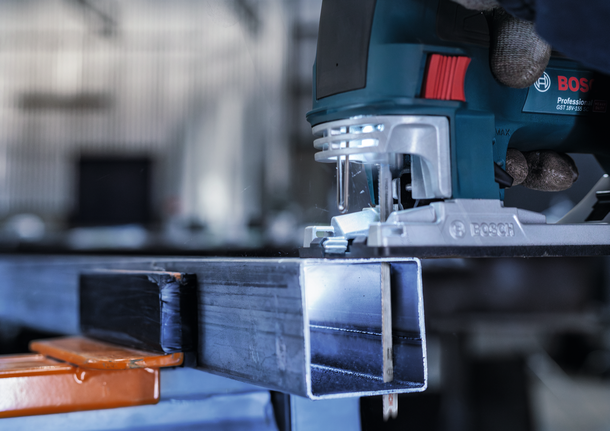 บุคคลที่สวมอุปกรณ์ความปลอดภัยกำลังนำจิ๊กซอว์ไปตัดผ่านคานโลหะ