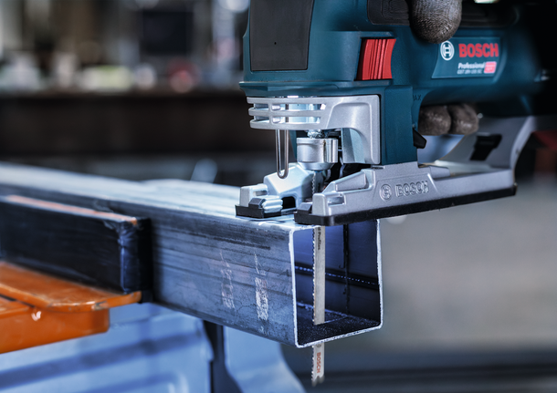 บุคคลที่สวมอุปกรณ์ความปลอดภัยกำลังตัดคานโลหะด้วยจิ๊กซอว์